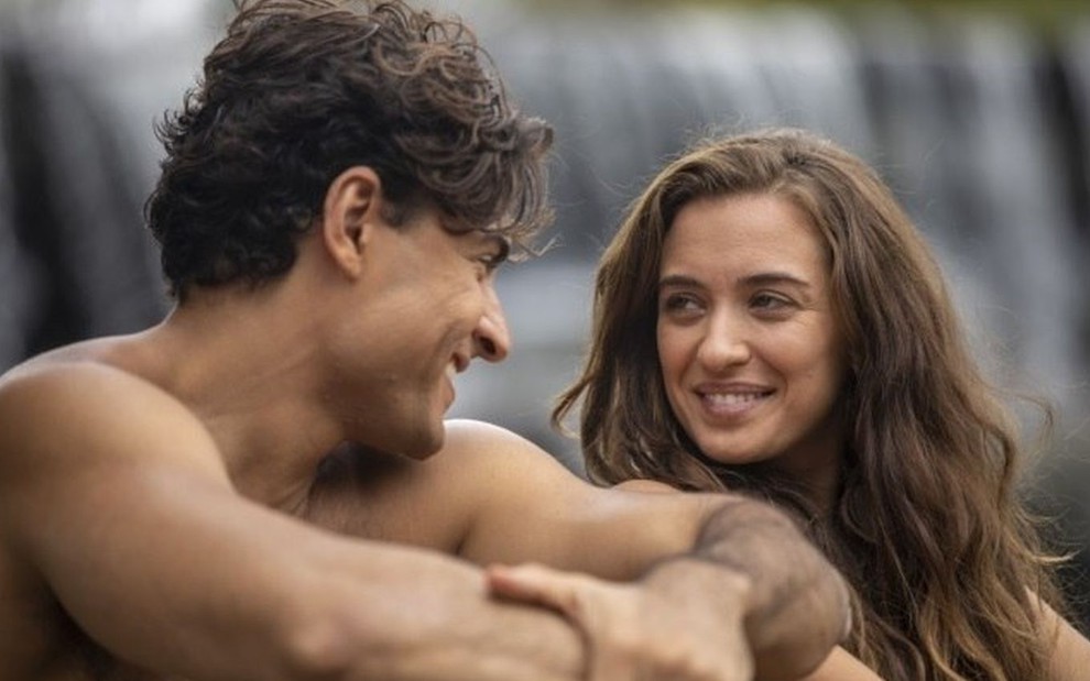 Adão (Carlo Porto) e Eva (Juliana Boller) olhando um para o outro em cena na cachoeira