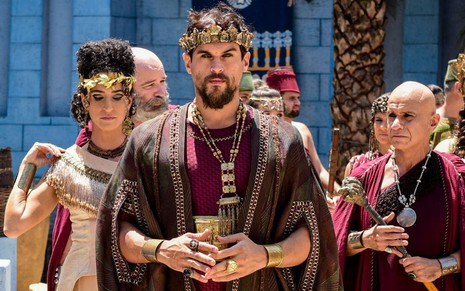 Felipe Roque (ao centro) como o rei Ibbi-Sim olha para a câmera em cena de Gênesis; ele está cercado por outras pessoas