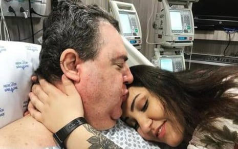 Gerson Brenner em uma cama de hospital com a filha, Vitória