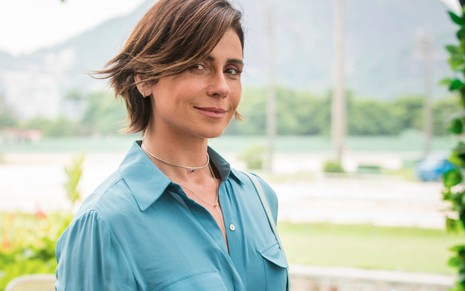 Giovanna Antonelli com leve sorriso e camisa azul, caracterizada como Lívia, sua personagem na série Filhas de Eva, do Globoplay