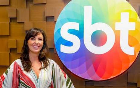 Glenda Kozlowski posa sorrindo em frente ao logo do SBT