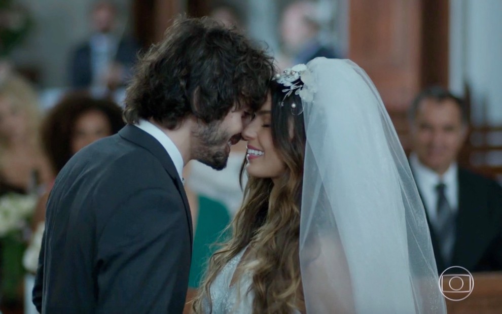De terno, o ator Fiuk encosta o rosto no de Isis Valverde, que está vestida de noiva em gravação da novela A Força do Querer