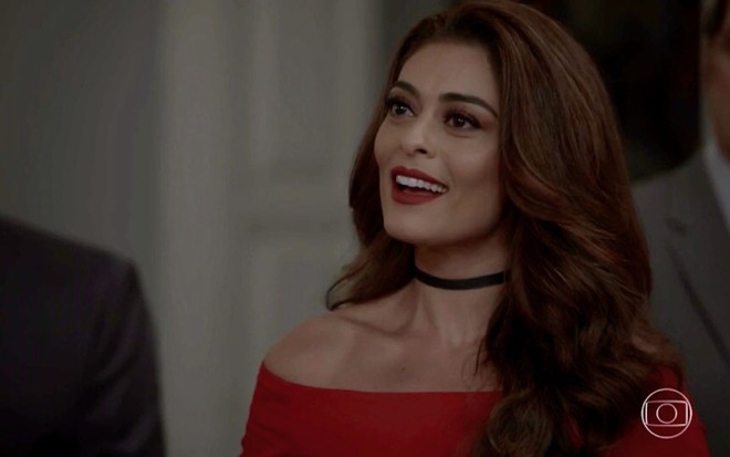 A atriz Juliana Paes, vestida de vermelho, conversa com alguém fora de quadro em cena da novela A Força do Querer