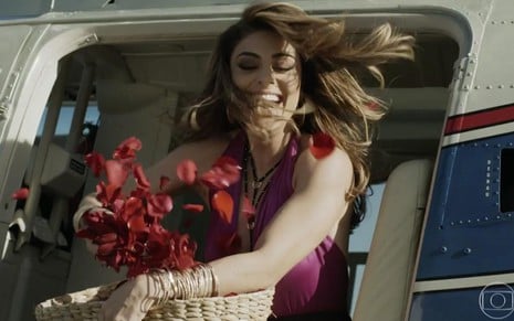 Juliana Paes em cena de A Força do Querer: morena tem cesta de pétalas de flores na mão e está a bordo de helicóptero