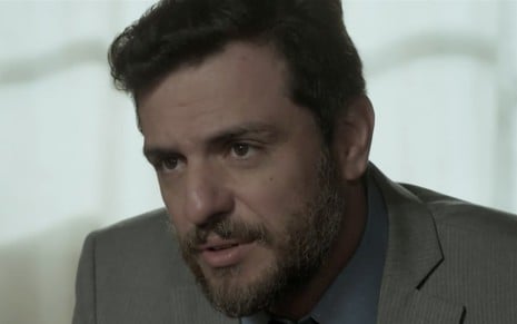 Rodrigo Lombardi caracterizado como Caio em A Força do Querer; sentado, ator olha de maneira séria para alguém fora do quadro