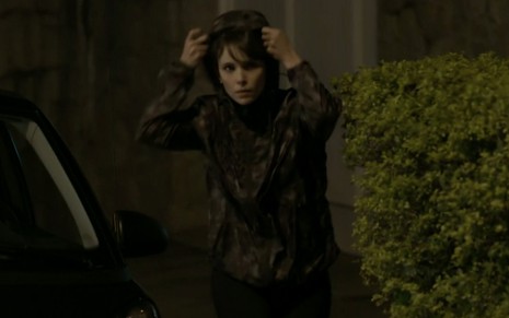 A atriz Débora Falabella veste um casaco camuflado com capuz e caracterizada como Irene em cena de A Força do Querer