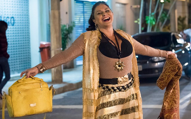 A cantora Fafá de Belém segura uma bolsa amarela e está vestida com uma roupa espalhafatosa como Almerinda em cena de A Força do Querer