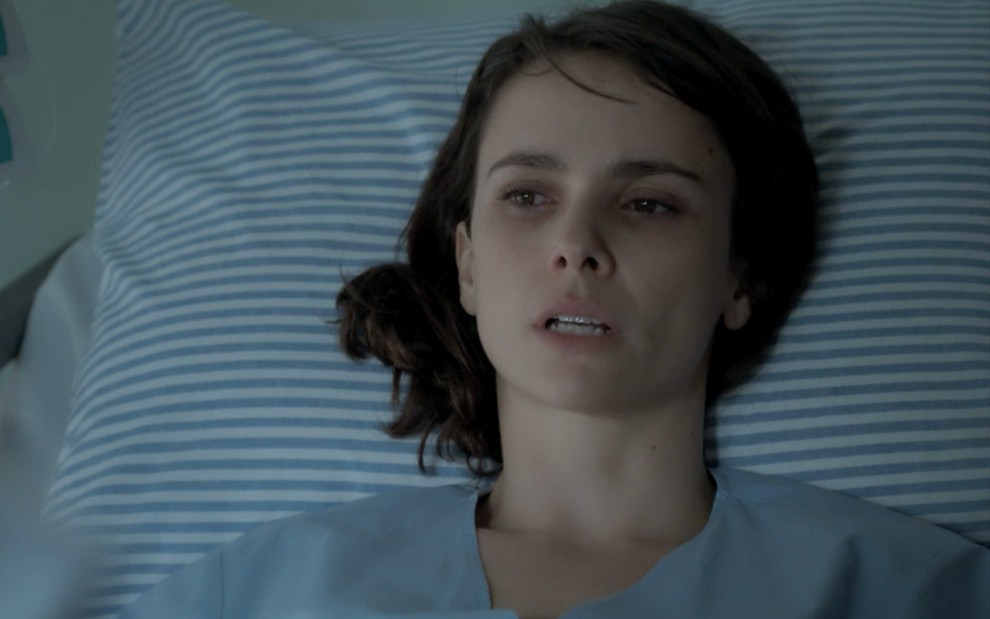 A atriz Débora Falabella, na cama de hospital com cara de doente, em cena como Irene em A Força do Querer