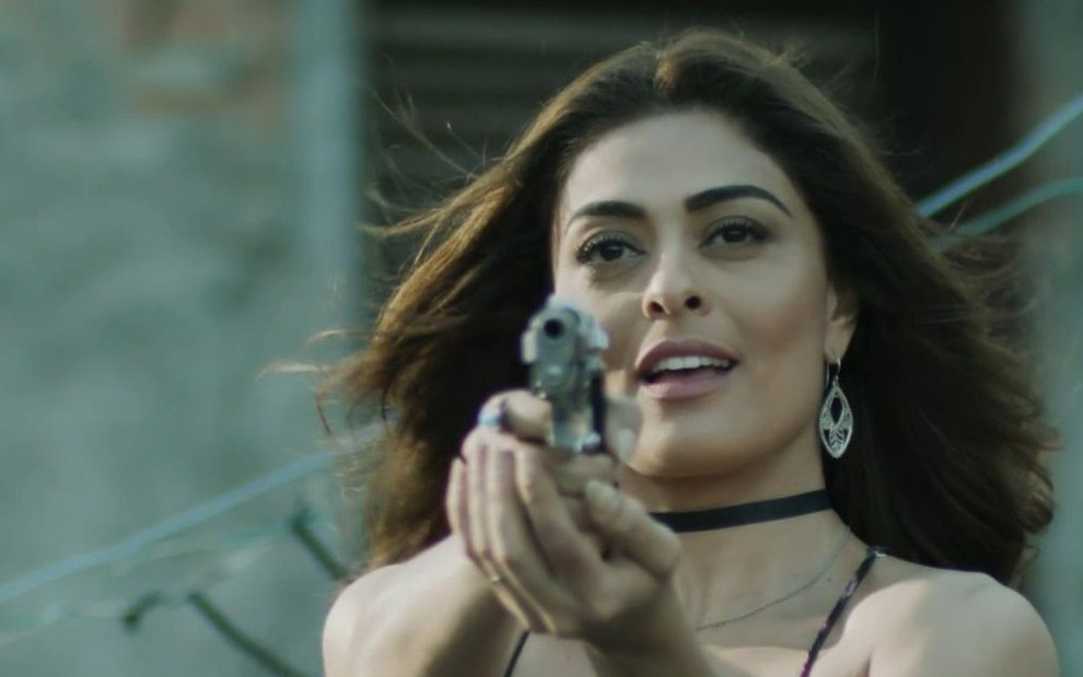 A atriz Juliana Paes segura um revólver com as duas mãos caracterizada como a Bibi em cena de A Força do Querer
