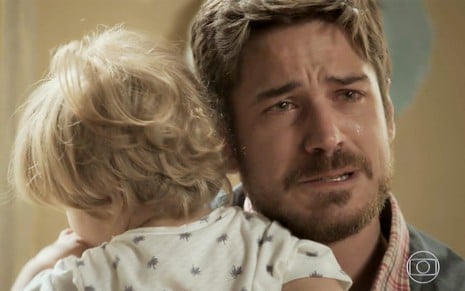 Lorenzo Souza e Marco Pigossi em cena de A Força do Querer: com a criança no colo, ator olha com emoção para alguém fora do quadro