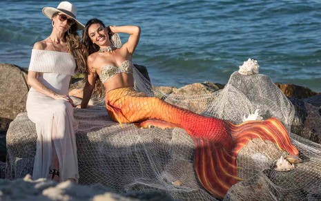 As atrizes Maria Fernanda Cândido e Isis Valverde, usando uma cauda de sereia, podem juntas na praia como Joyce e Ritinha em A Força do Querer
