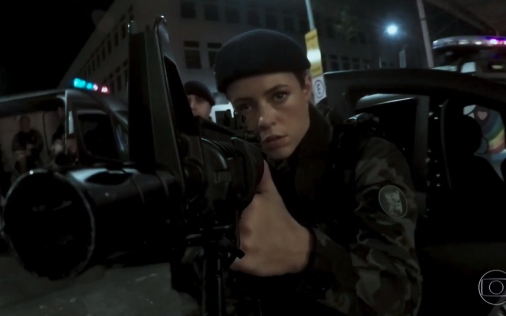 A atriz Paolla Oliveira, vestida de policial e segurando uma arma, em cena como Jeiza em A Força do Querer