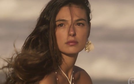 Isis Valverde em cena de A Força do Querer: personagem está na beira da praia e olha com curiosidade para alguém fora do quadro