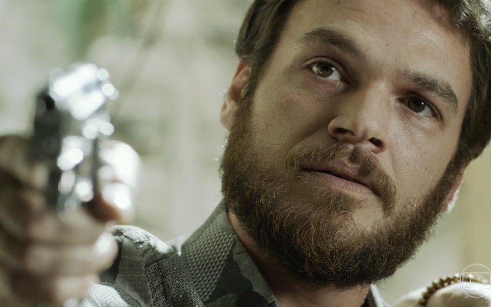Emilio Dantas caracterizado como Rubinho em A Força do Querer: com close, personagem segura arma e encara alguém de fora do quadro