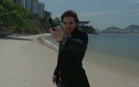 Fiuk em cena de A Força do Querer: caracterizado como Ruy, personagem aponta pistola para alguém fora do quadro