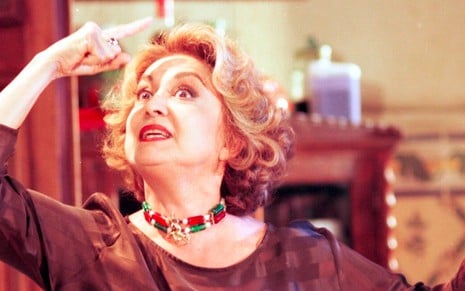 A atriz Eva WIlma com dedo em riste segura um galho caracterizada como a Maria Altiva em cena de A indomada