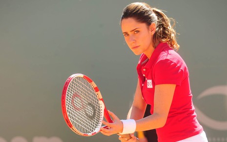 Fernanda Vasconcellos em cena de A vida da Gente: caracterizada como Ana, atriz está com uniforme de tênis e segura uma raquete com uma das mãos