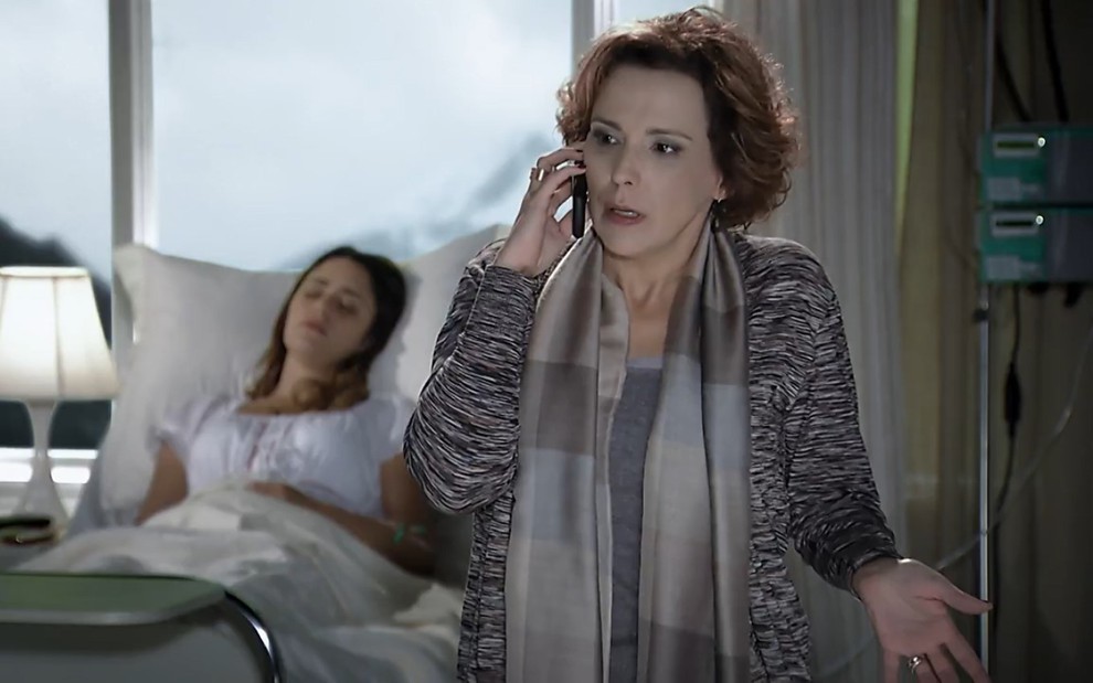 Ana Beatriz Nogueira vestida de cinza ao telefone e Fernanda Vasconcellos deitada em segunda plano na imagem