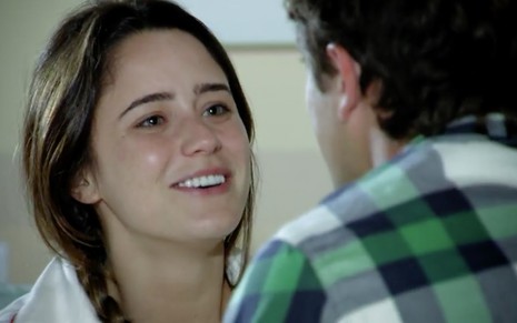 A atriz Fernanda Vasconcellos como Ana sentada em uma cama olha para Rafael Cardoso, que está de costas como Rodrigo, e sorri em cena de A Vida da Gente