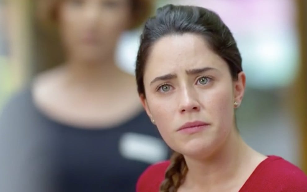 A atriz Fernanda Vasconcellos está de pé, com um olhar triste, como Ana em cena de A Vida da Gente