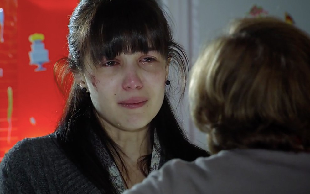 A atriz Marjorie Estiano, com machucados no rosto, tem expressão de choro e está caracterizada como Manuela em cena de A Vida da Gente