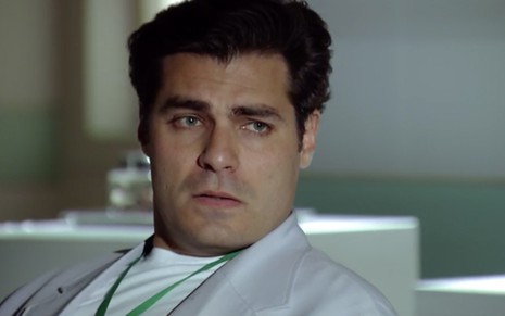 O ator Thiago Lacerda como Lúcio está de jaleco branco, sentado em uma poltrona na sala de espera de um hospital, em cena de A Vida da Gente
