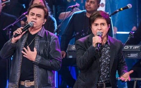 Chitãozinho & Xororó em apresentação, ambos estão cantando e com um microfone na mão