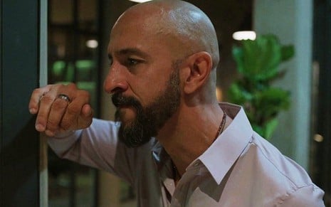 O ator Irandhir Santos encena momento de reflexão em que seu personagem encosta a mão em uma parede em Amor de Mãe