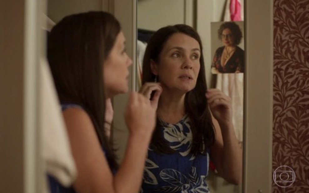 A atriz Adriana Esteves como Thelma conversa com uma foto de Isabel Teixeira presa na parte superior do armário de seu quarto em cena de Amor de Mãe
