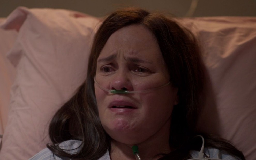 Thelma (Adriana Esteves) chora deitada em uma cama de hospital em cena de Amor de Mãe
