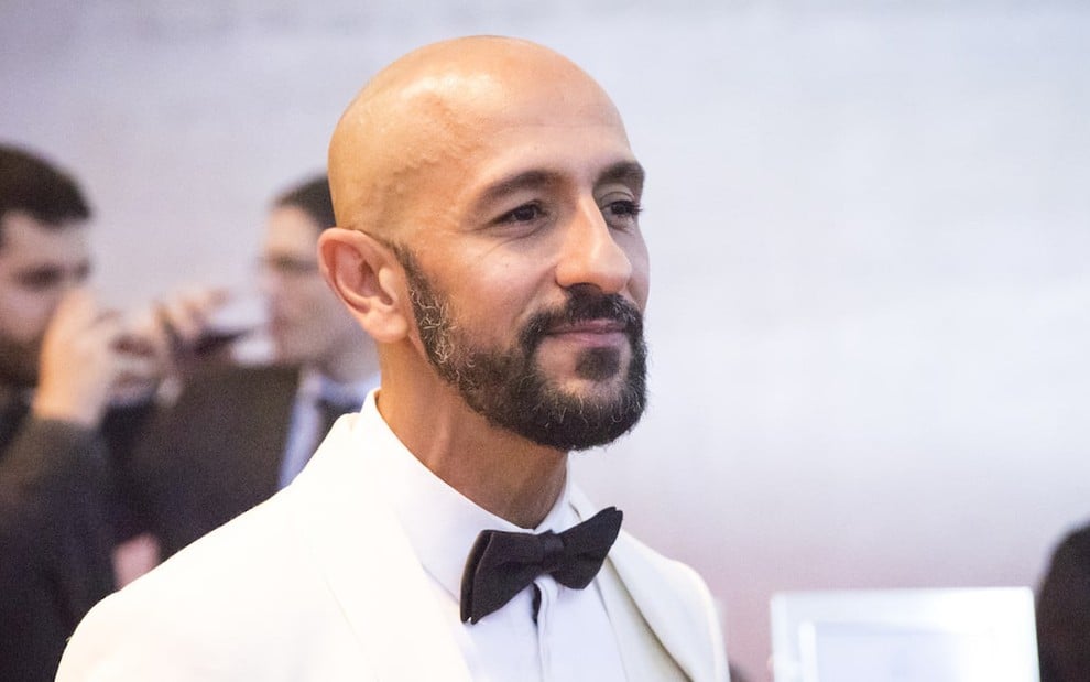 O ator Irandhir Santos usa smoking branco com gravata borboleta preta em cena da novela Amor de Mãe, da TV Globo