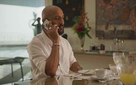 Irandhir Santos grava de camisa branca e falando ao telefone como Álvaro em Amor de Mãe