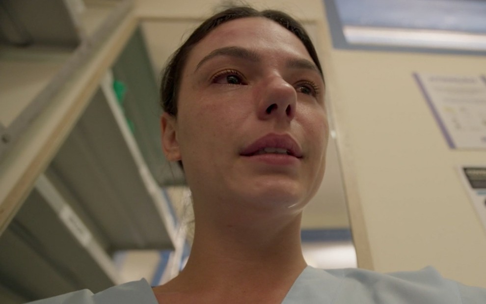 Isis Valverde em cena de Amor de Mãe: com uniforme de enfermeira, atriz é vista debaixo e tem marcas de máscara protetora no rosto