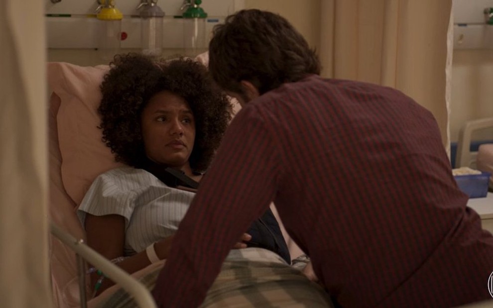 Jéssica Ellen deitada em leito de hospital conversa com Chay Suede (de costas) em cena da novela das nove da TV Globo