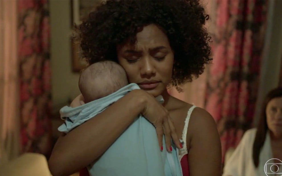 Jéssica Ellen em cena de Amor de Mãe: caracterizada como Camila, atriz segura bebê no colo e está com os olhos fechados