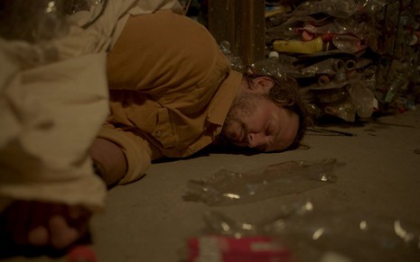 Vladimir Brichta grava caído no chão desacordado rodeado de materiais recicláveis em cena como Davi de Amor de Mãe