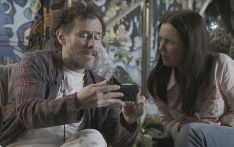 O ator Enrique Diaz mostra celular para Adriana Esteves em cena da novela Amor de Mãe, em que os dois interpretam os amigos Durval e Thelma