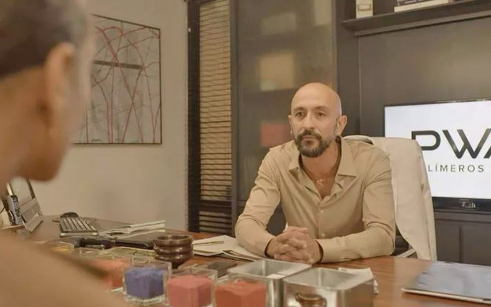 Taís Araújo está de costas, como a Vitória, diante de Irandhir Santos, que interpreta o Álvaro, os dois estão conversando em uma sala da empresa PWA em cena de Amor de Mãe