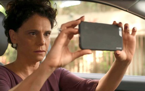 A atriz Malu Galli segura um celular e simula fazer imagens com o aparelho em cena da novela Amor de Mãe, da TV Globo