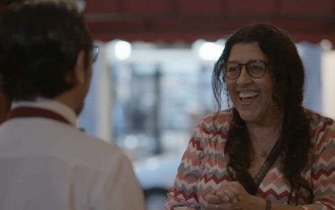 Nanego Lira (de costas) contracena com Regina Casé, que abre um sorriso enorme para o pretendente na novela Amor de Mãe