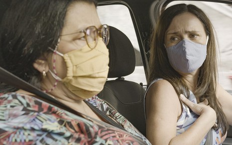 Sentadas em um carro, Regina Casé e Adriana Esteves gravam cena de Amor de Mãe gravando máscaras