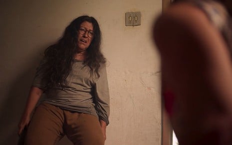 Lurdes (Regina Casé) chora encostada na parede com um pau na mão em cena de Amor de Mãe