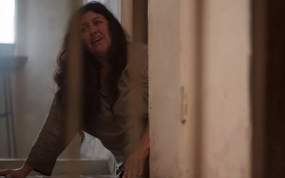 A atriz Regina Casé como Lurdes está atrás das grades, deitada no chão, com expressão de sofrimento em cena de Amor de Mãe