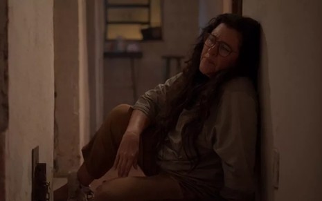 A atriz Regina Casé, sentada no chão, em cena como Lurdes em Amor de Mãe