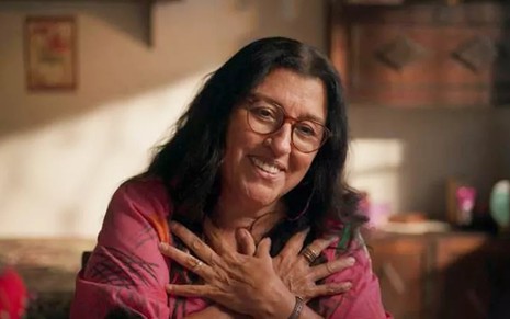 A atriz Regina Casé, com as mãos cruzadas no peito, em cena como Lurdes, em Amor de Mãe