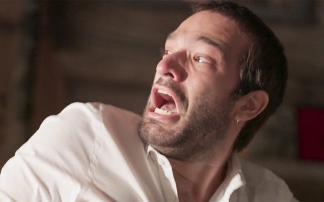 Humberto Carrão em cena de Amor de Mãe: caracterizado como Sandro, personagem grita e olha com desespero para alguém fora do quadro