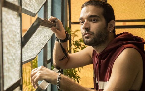 O ator Humberto Carrão olha pela janela em cenário da novela Amor de Mãe, da TV Globo, na qual interpreta Sandro