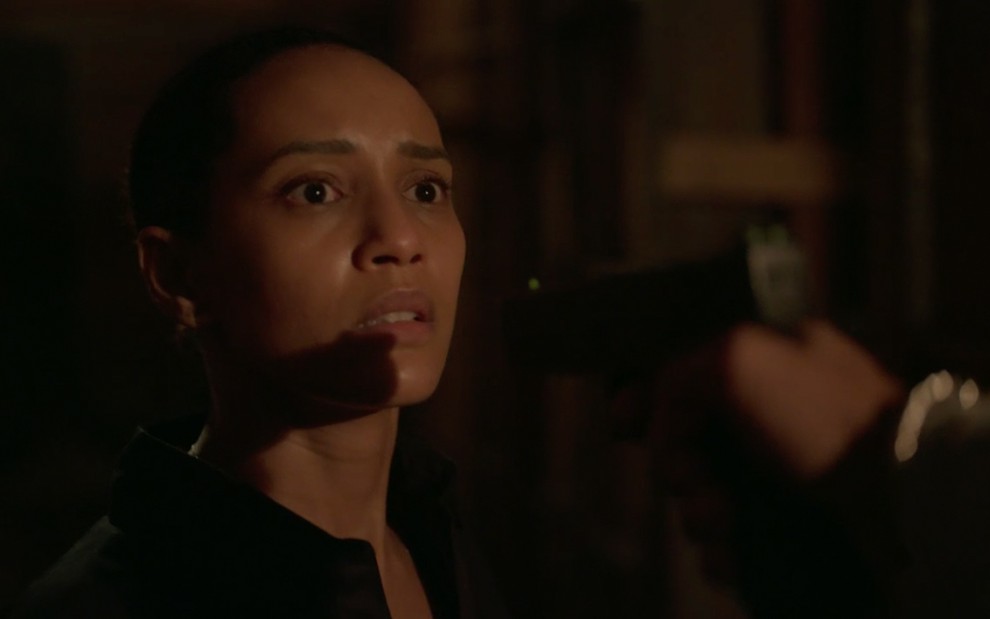 A atriz Taís Araujo caracterizada como Vitória em um beco escuro com um revólver apontado para a sua cabeça em cena de Amor de Mãe