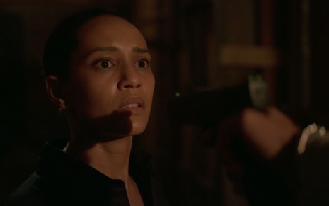 A atriz Taís Araujo caracterizada como Vitória em um beco escuro com um revólver apontado para a sua cabeça em cena de Amor de Mãe