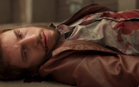 O ator Rodrigo Garcia com olhos abertos e sangue escorrendo pela boca em cena da morte de seu personagem em Amor de Mãe